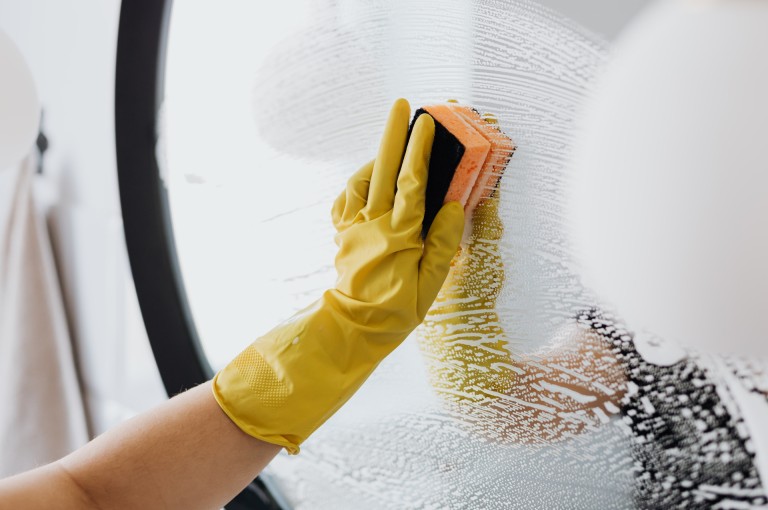 Professional spring cleaning service removing winter grime and dust from a bathroom mirror for a fresh seasonal home reset